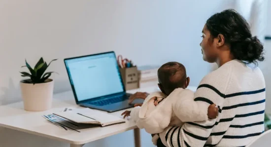 Como conciliar maternidade e pós-graduação? | Foto de mulher segurando um bebê enquanto mexe no notebook | FAVENI