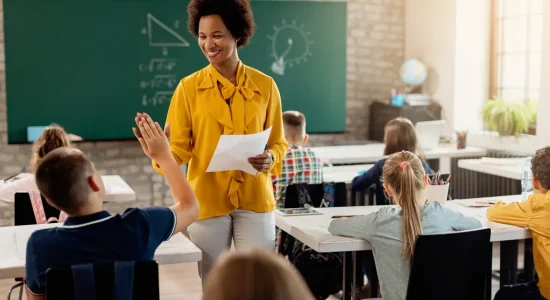 Happy African American teacher giving high-five to elementary student and congratulating him on good test results.