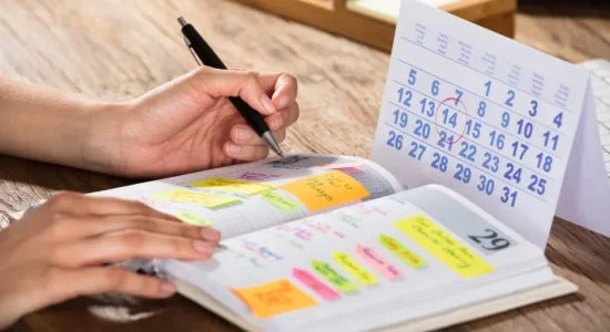 Flexibilidade na pós-graduação EaD: como gerenciar o estudo? | Pessoa anotando compromissos em uma agenda olhando um calendário | FAVENI